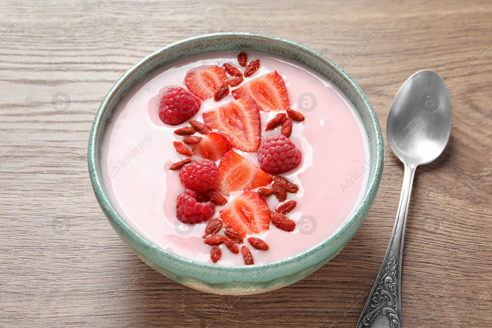 Photo of Smoothie bowl with goji berries and spoon on wooden table