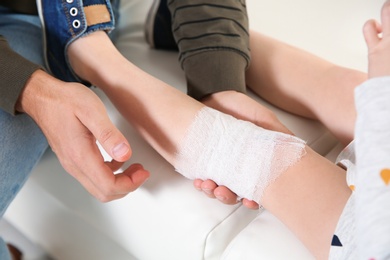 Photo of Father applying bandage on daughter's injured knee at home, closeup. First aid