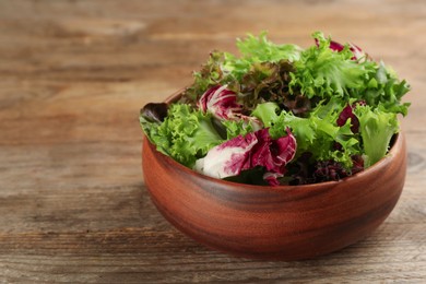 Bowl with different sorts of lettuce on wooden table. Space for text