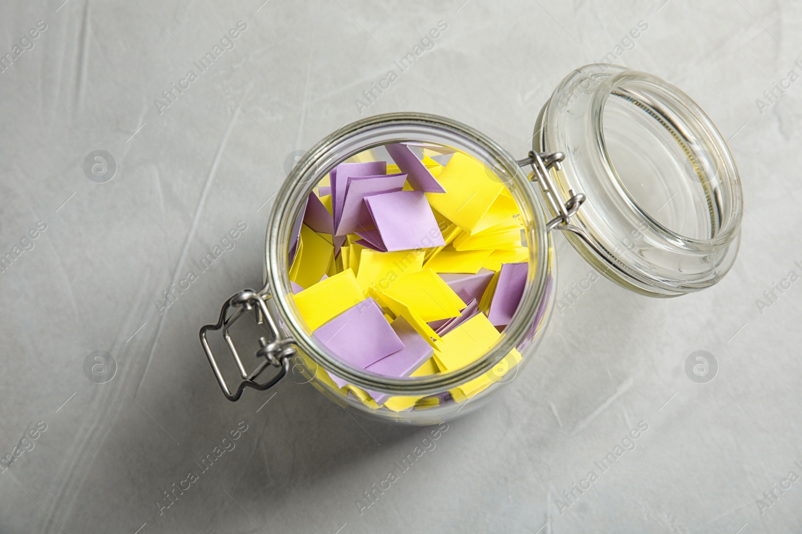 Photo of Colorful paper pieces for lottery in glass jar on table, top view