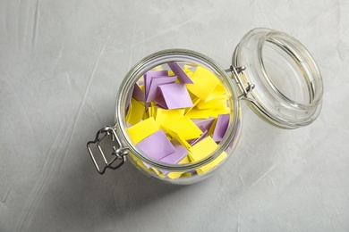 Colorful paper pieces for lottery in glass jar on table, top view