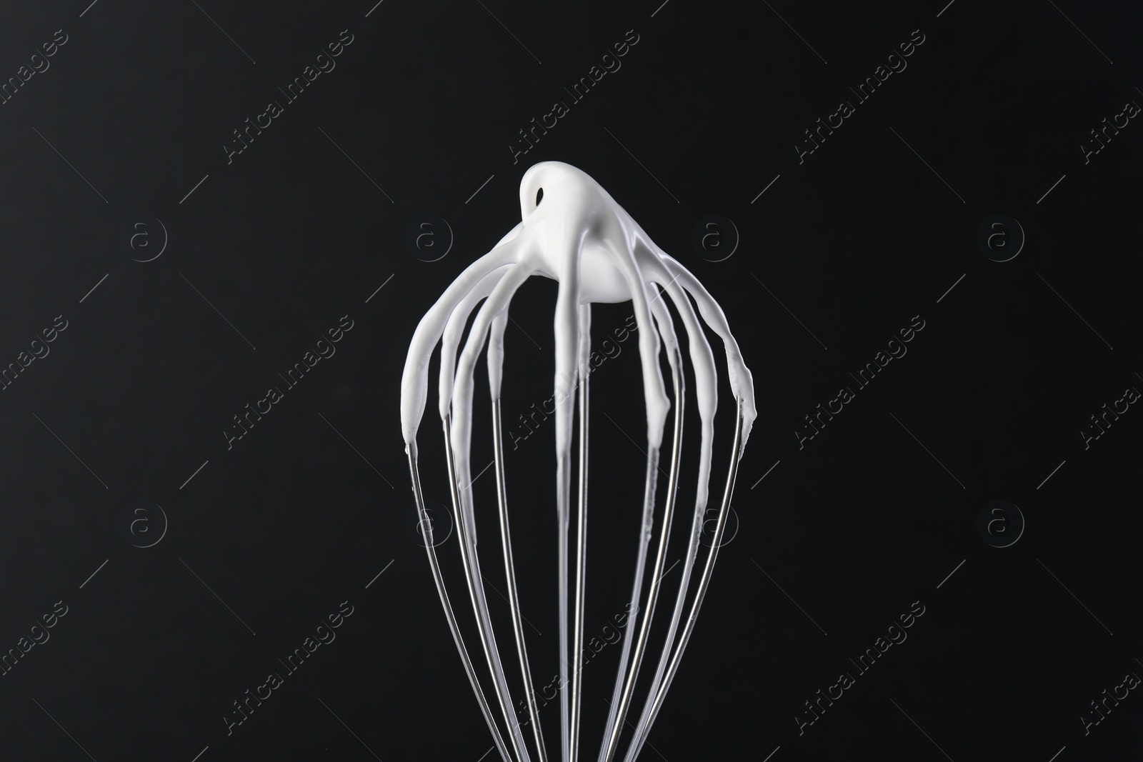 Photo of Whisk with whipped cream on black background, closeup
