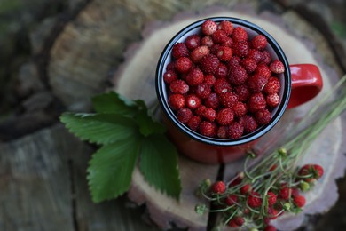 Photo of Mug, tasty wild strawberries and green leaves on stump, above view