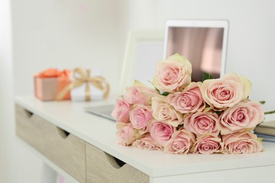 Photo of Beautiful bouquet of roses and gifts near laptop on white table. Happy birthday greetings