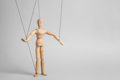 Photo of One wooden puppet with strings on light grey background. Space for text