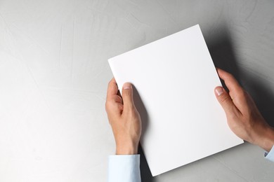 Photo of Man holding blank notebook at light grey table, top view. Mockup for design