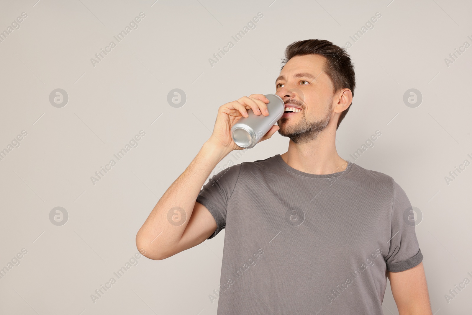 Photo of Happy man drinking from tin can on light grey background. Space for text