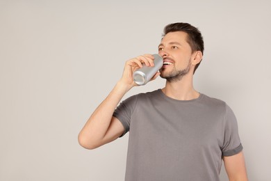 Photo of Happy man drinking from tin can on light grey background. Space for text