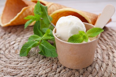 Photo of Paper cup with ice cream and mint leaves on wicker mat