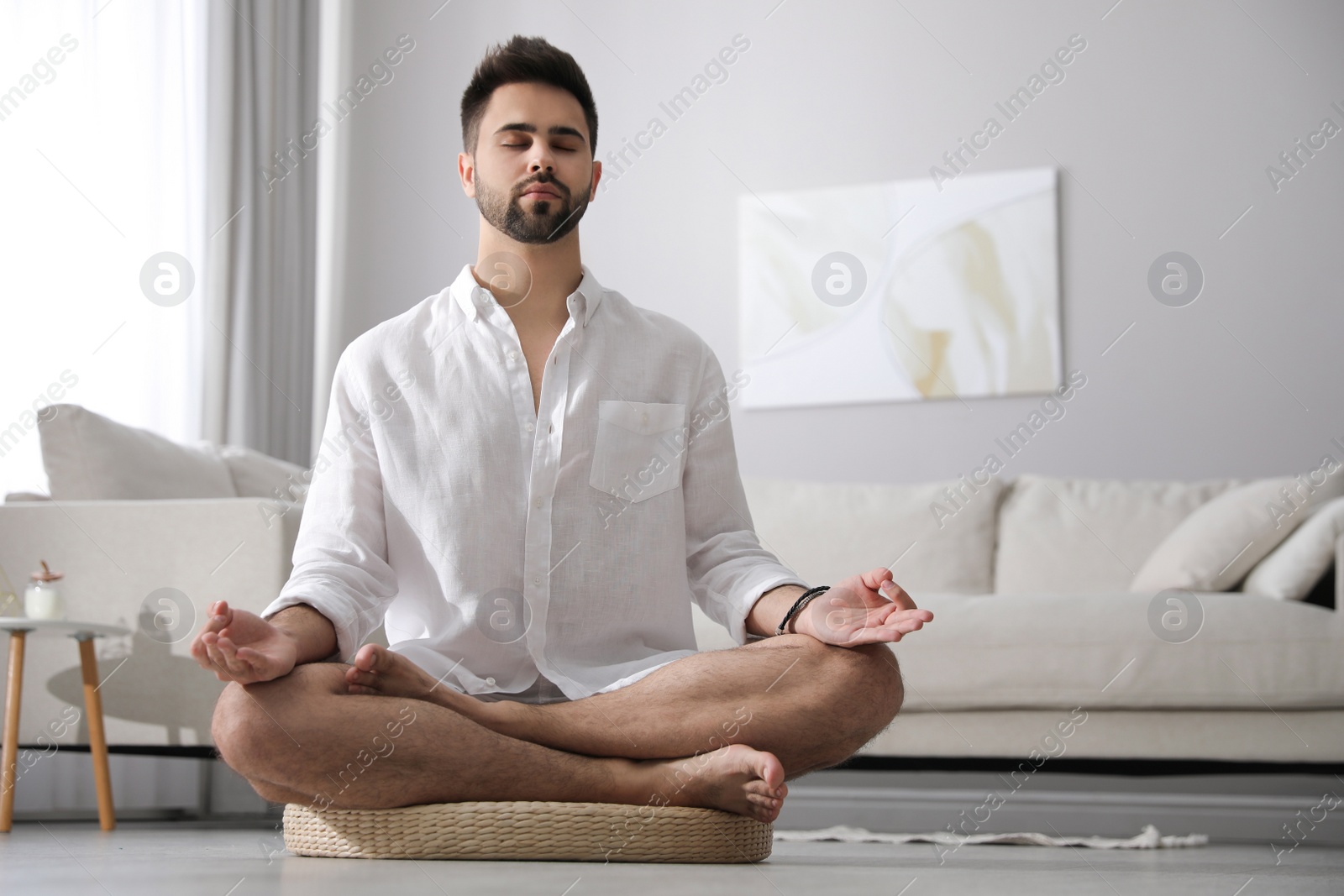 Photo of Young man meditating on straw cushion at home, space for text