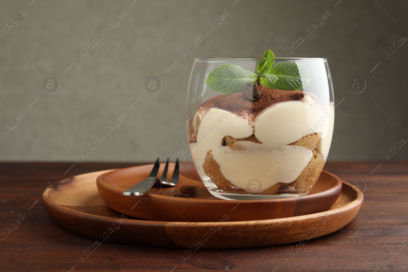 Photo of Delicious tiramisu in glass, mint leaves, coffee beans and fork on wooden table