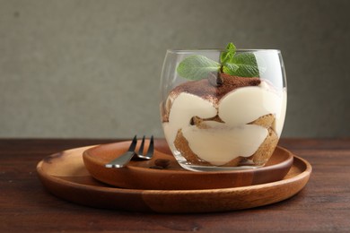 Delicious tiramisu in glass, mint leaves, coffee beans and fork on wooden table