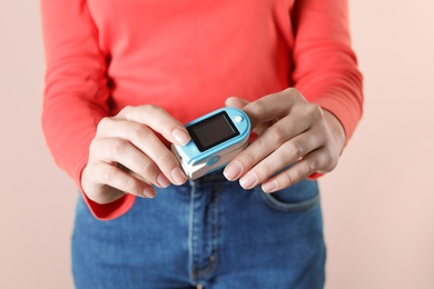 Young woman checking pulse with digital medical device on color background, closeup