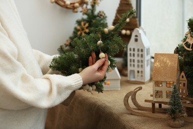 Photo of Woman holding small Christmas tree with wooden decorations near window sill indoors, closeup