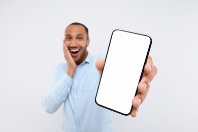 Surprised man showing smartphone in hand on white background, selective focus. Mockup for design