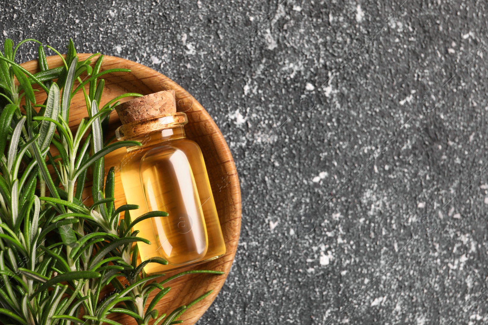 Photo of Bottle with essential oil and fresh rosemary on grey textured table, top view. Space for text