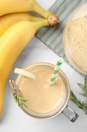 Mason jar of tasty banana smoothie with straw and fresh fruits on white marble table, flat lay