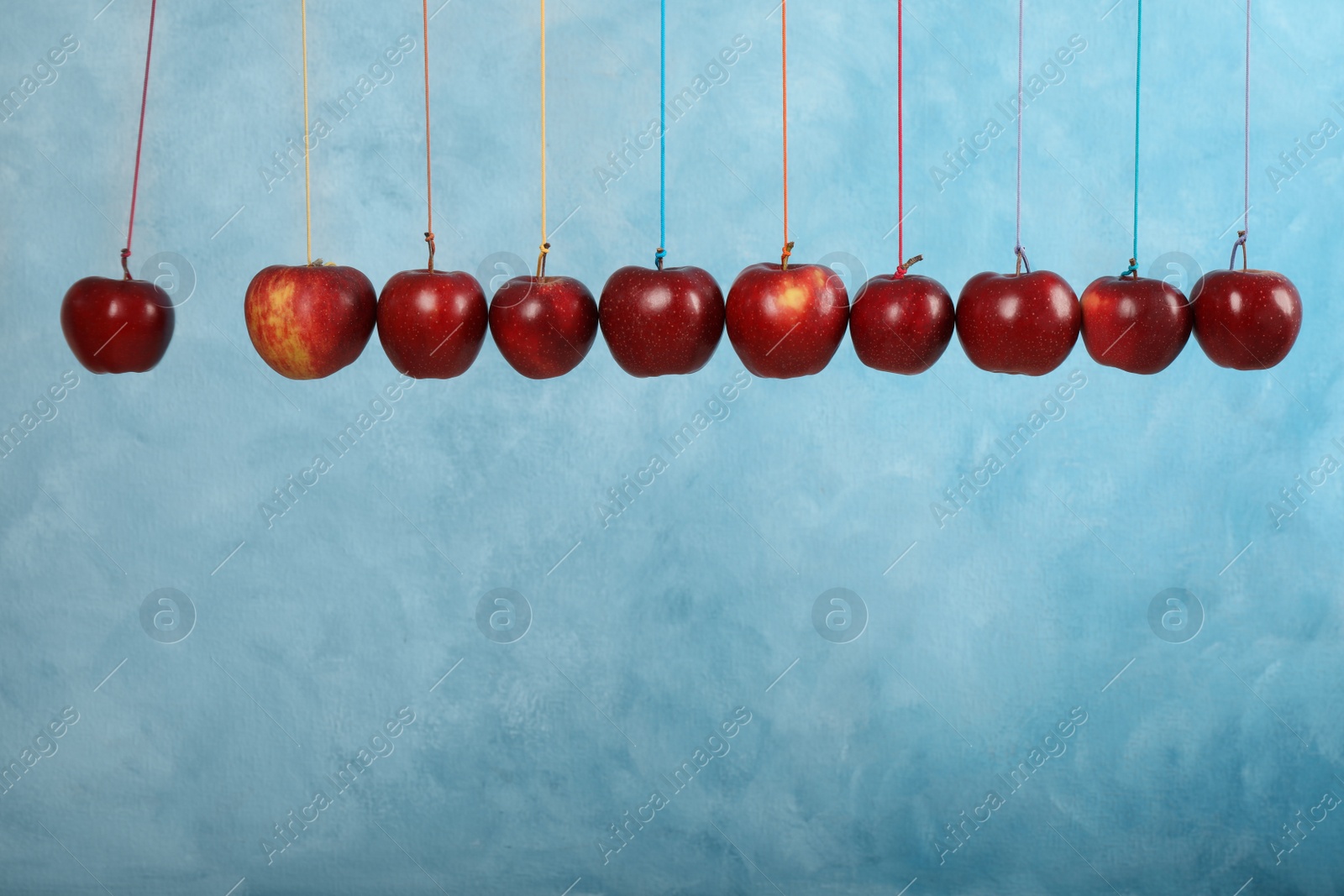 Photo of Ripe red apples hanging on light blue background, space for text