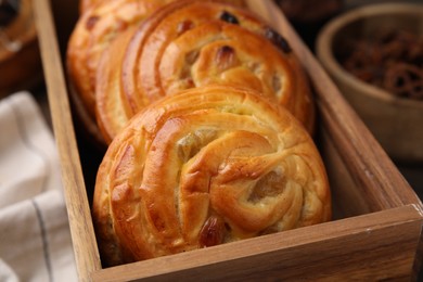 Delicious rolls with raisins in wooden box on table, closeup. Sweet buns