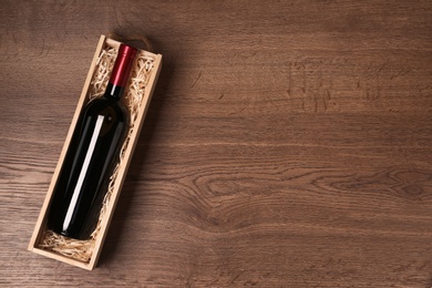 Open wooden crate with bottle of wine on table, top view. Space for text