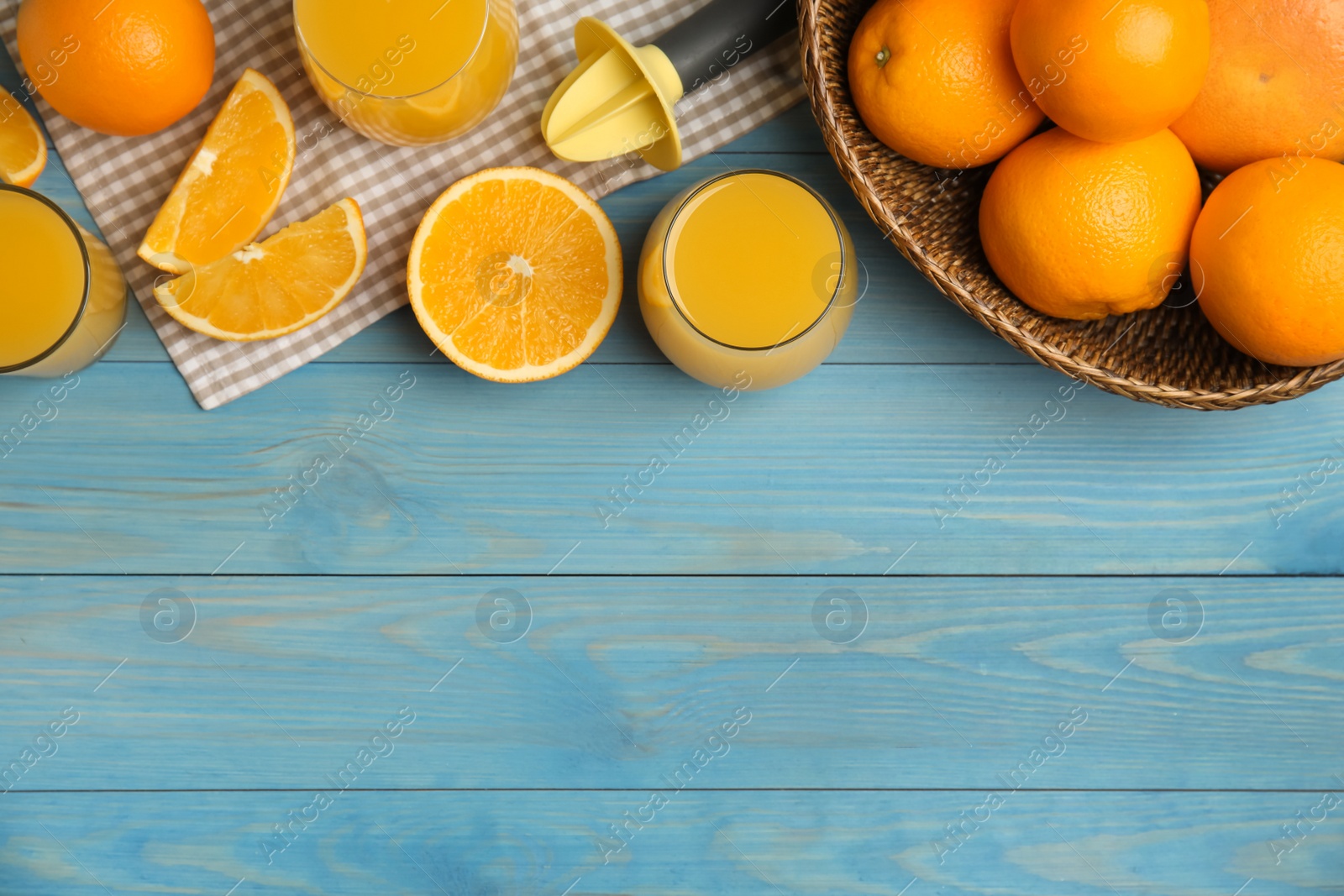 Photo of Freshly made juice, oranges and reamer on blue wooden table, flat lay. Space for text