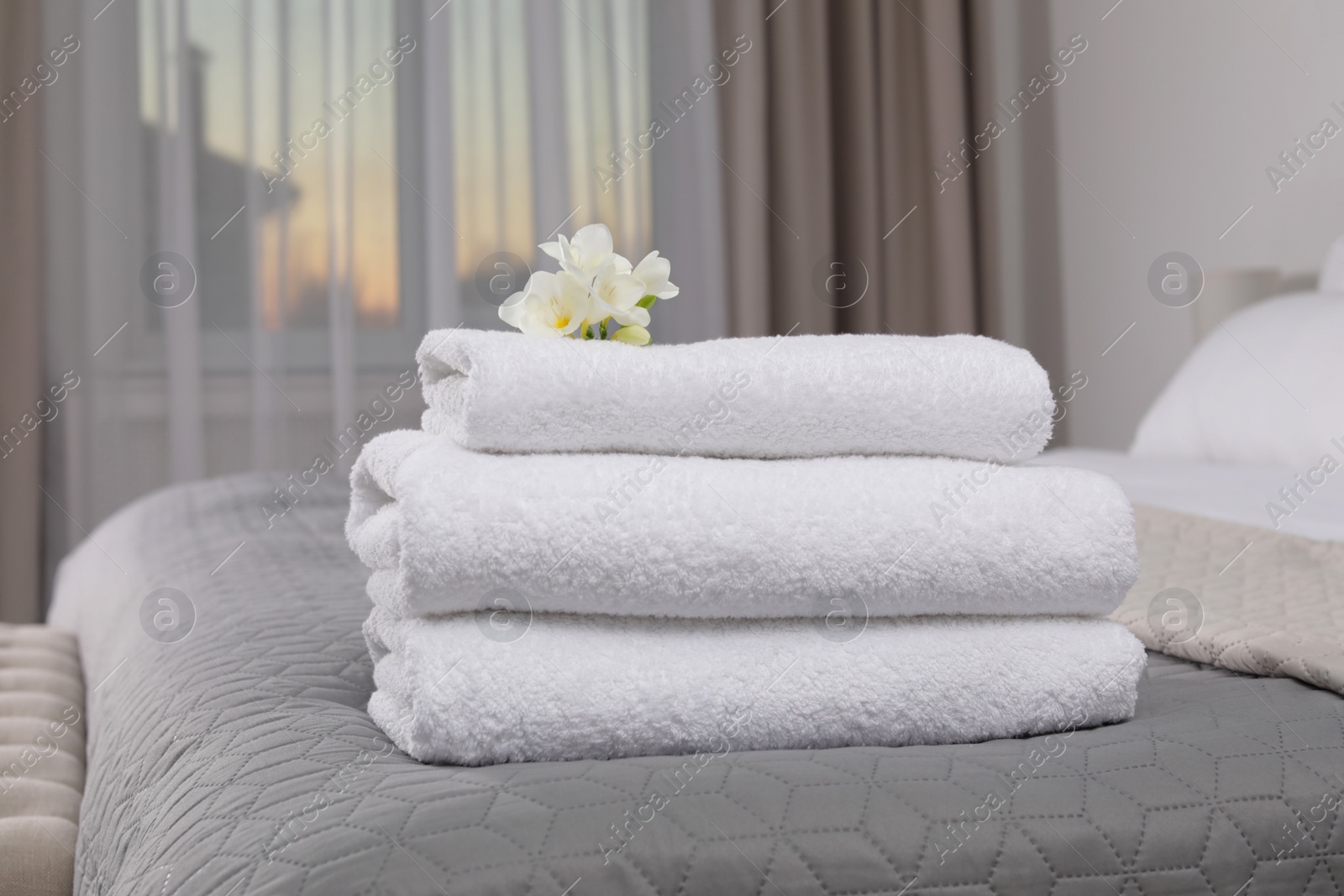Photo of Stack of fresh towels with flowers on bed in hotel room