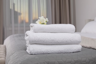 Stack of fresh towels with flowers on bed in hotel room