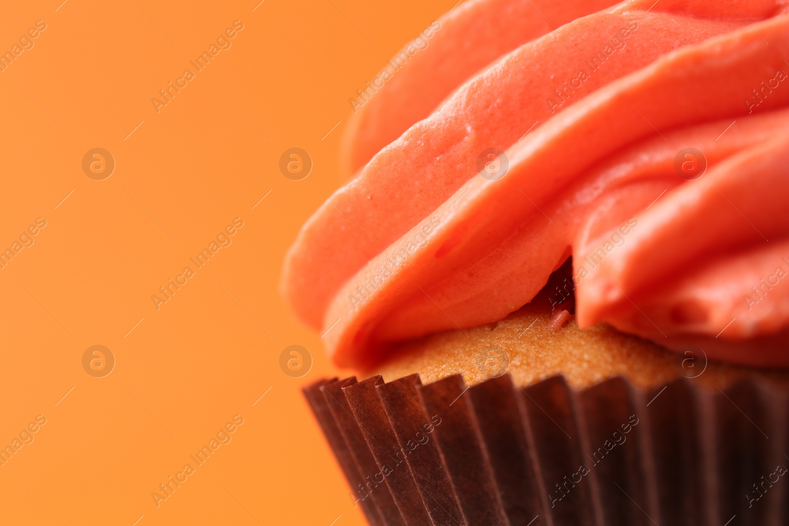 Photo of Delicious cupcake with bright cream on orange background, closeup. Space for text