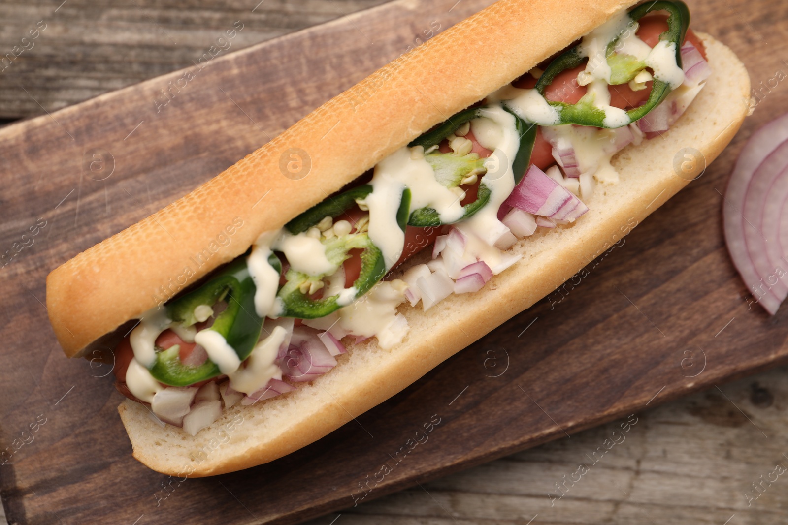 Photo of Delicious hot dog with onion, chili pepper and sauce on wooden table, top view