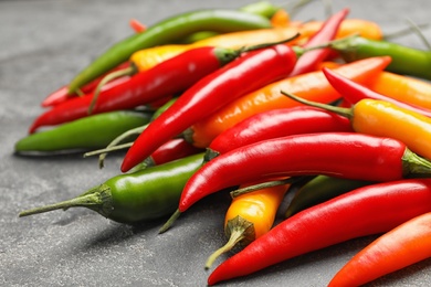 Photo of Different ripe chili peppers on grey table, closeup