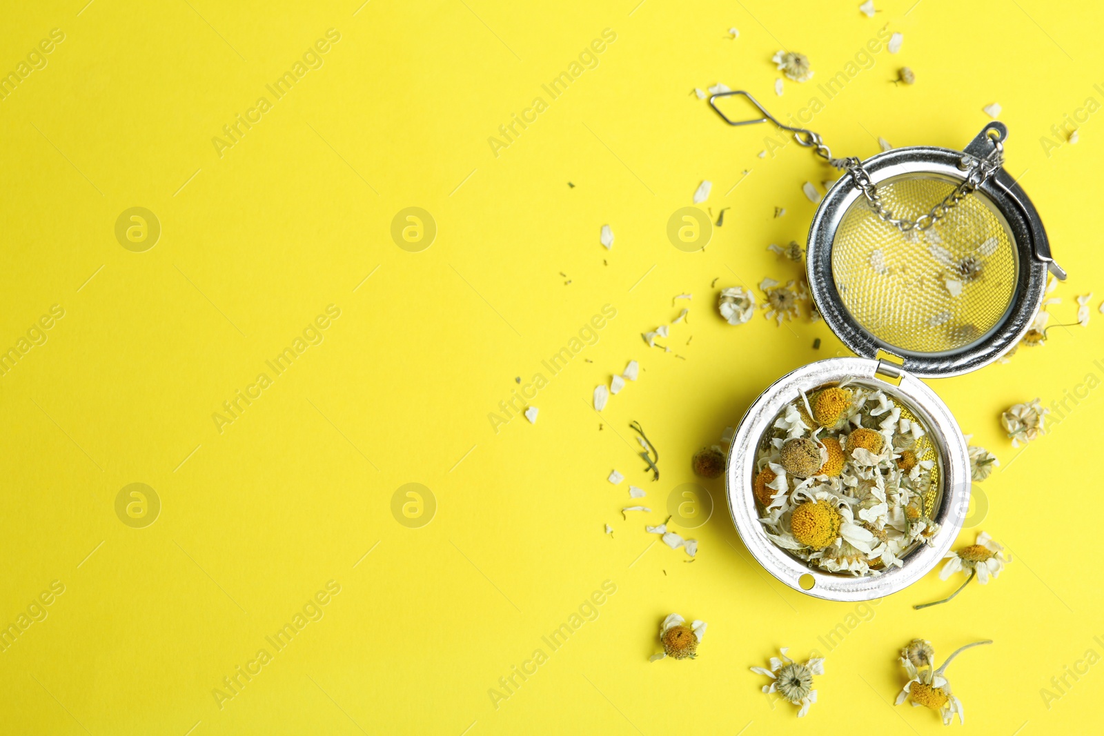 Photo of Dry chamomile flowers in infuser on yellow background, flat lay. Space for text