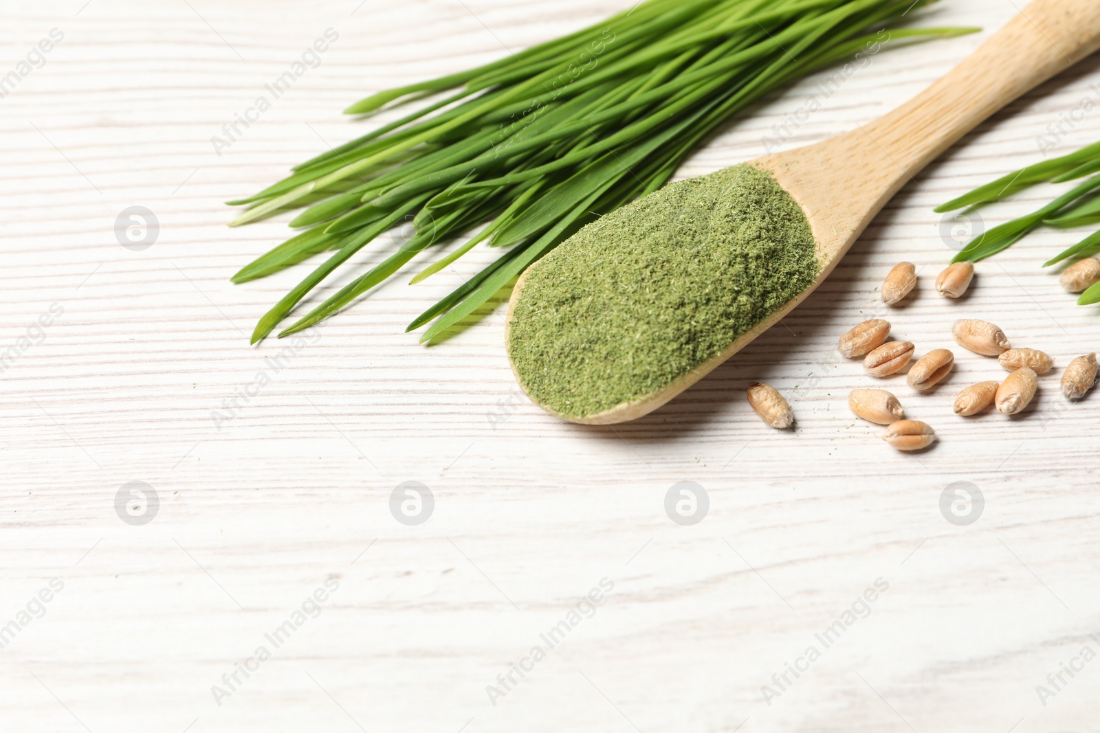 Photo of Wheat grass powder in spoon, seeds and fresh sprouts on white wooden table, space for text