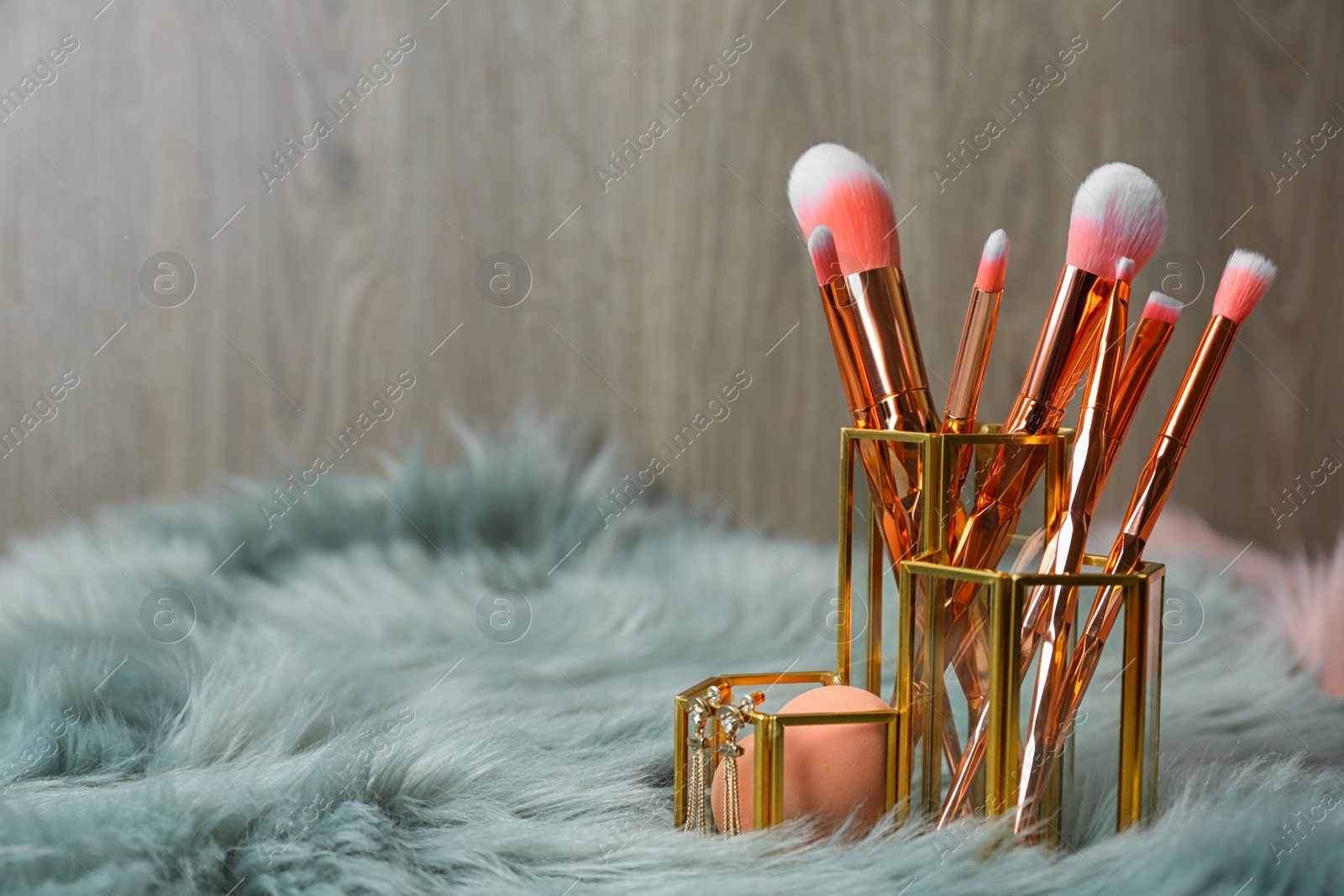 Photo of Organizer with set of professional makeup brushes and accessories on furry fabric against wooden background. Space for text