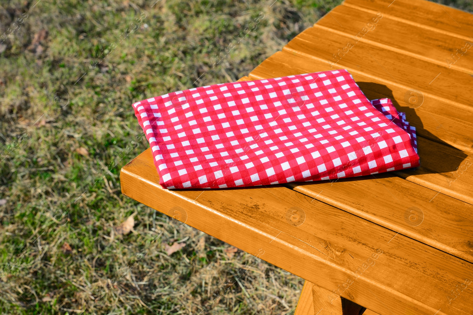 Photo of Folded red and white checkered tablecloth on wooden picnic table in park