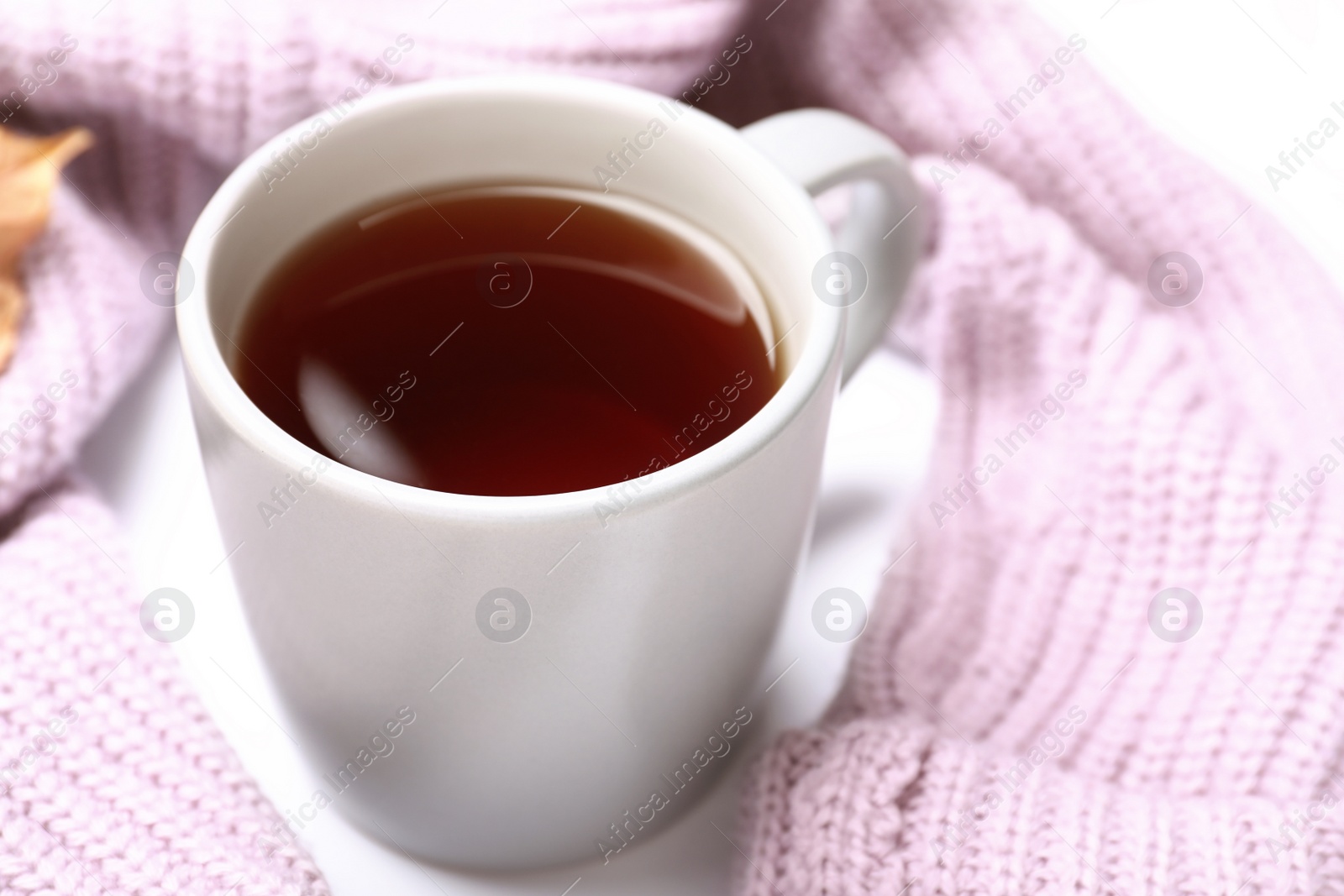 Photo of Cup of hot drink and knitted sweater on white table, closeup. Cozy autumn atmosphere