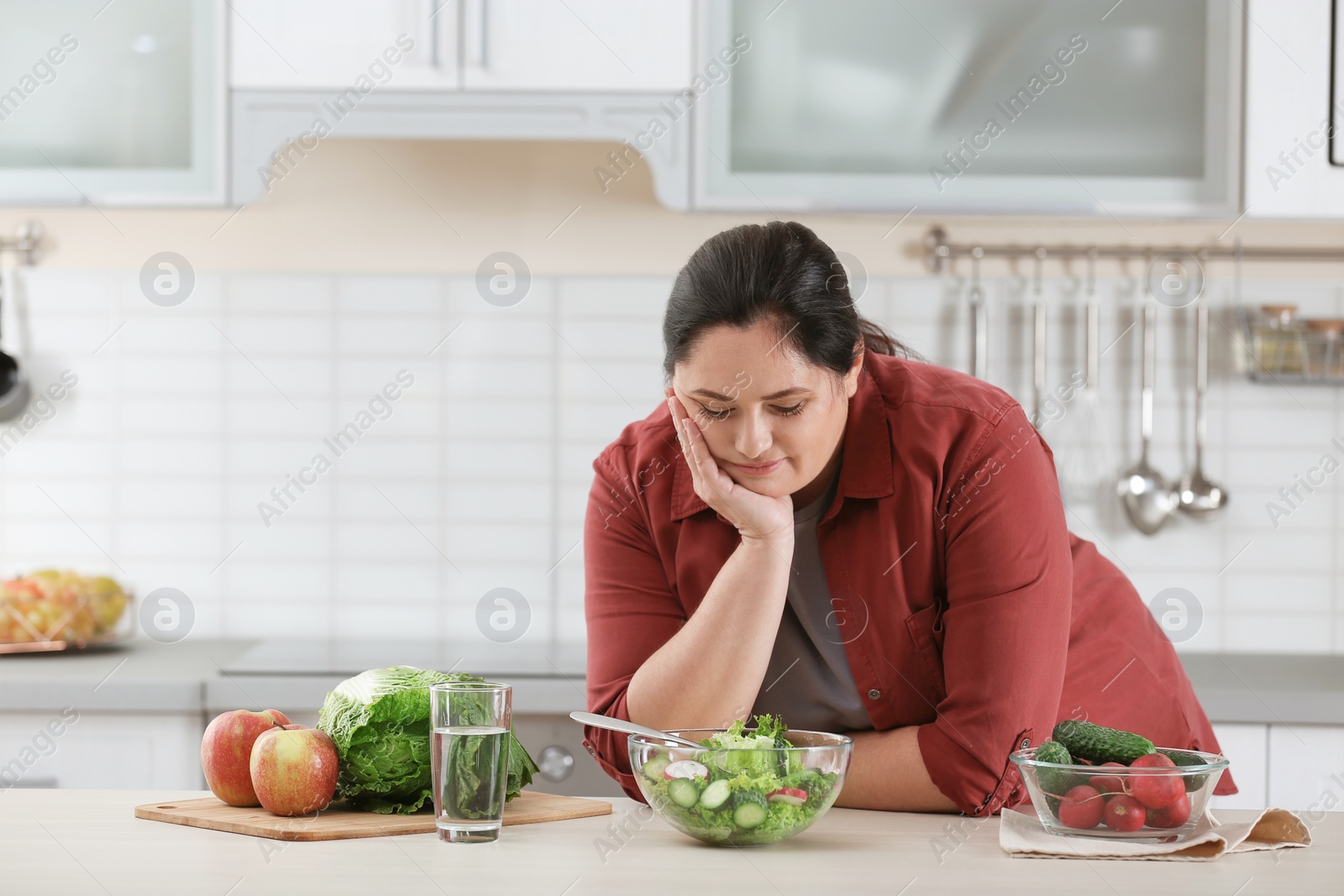 Photo of Unhappy woman with vegetable salad at table in kitchen. Healthy diet