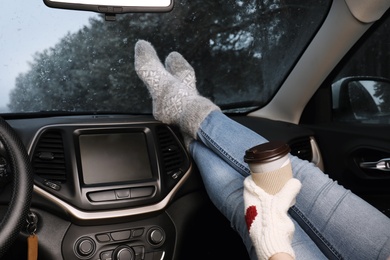 Photo of Woman in warm socks with coffee resting inside car, closeup