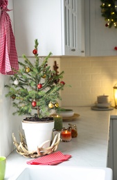 Small Christmas tree decorated with baubles and festive lights in kitchen