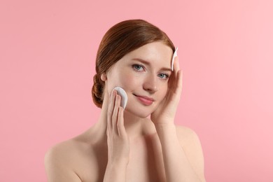 Beautiful woman with freckles wiping face on pink background