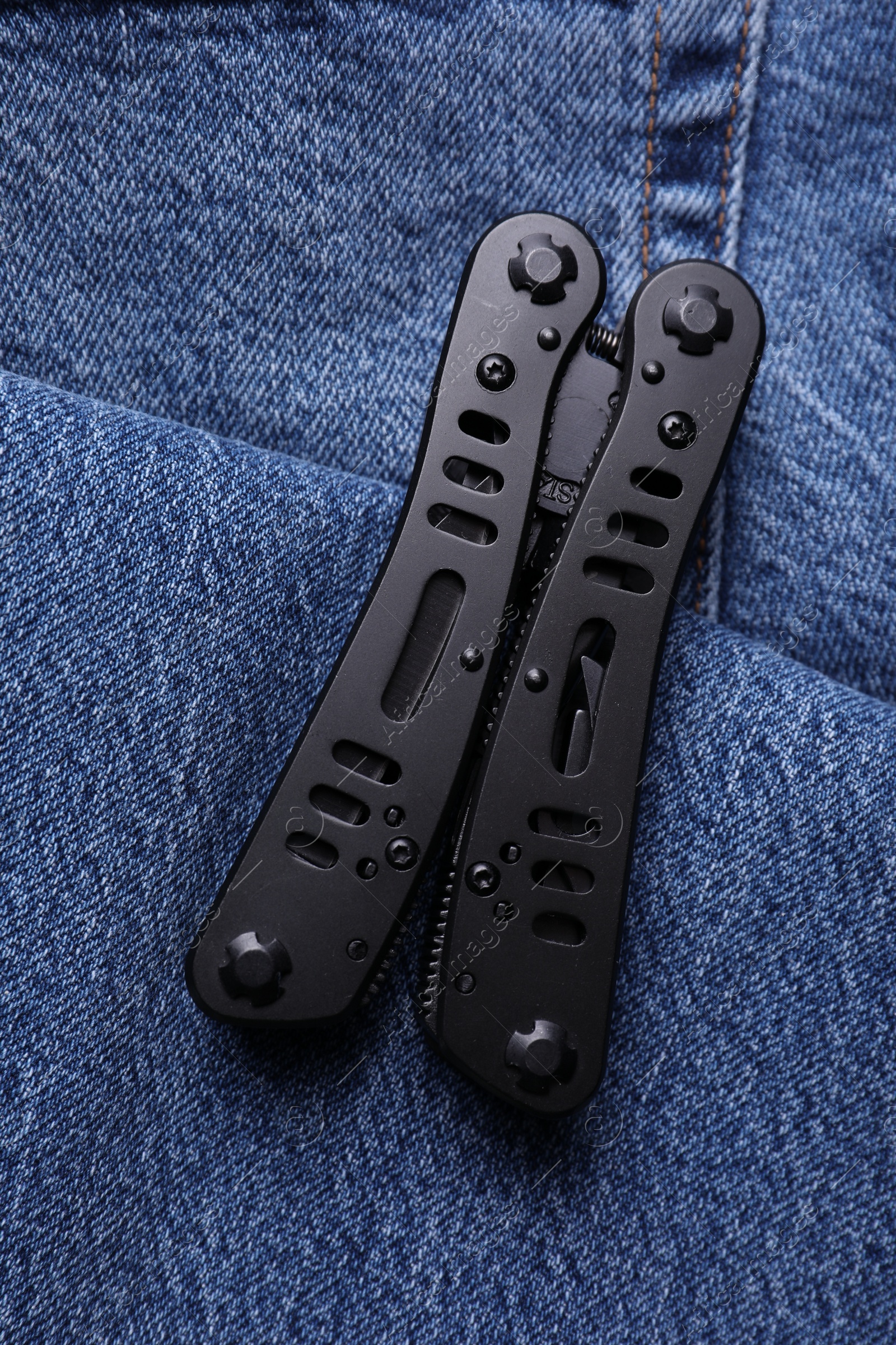 Photo of Modern compact portable multitool on denim fabric, top view