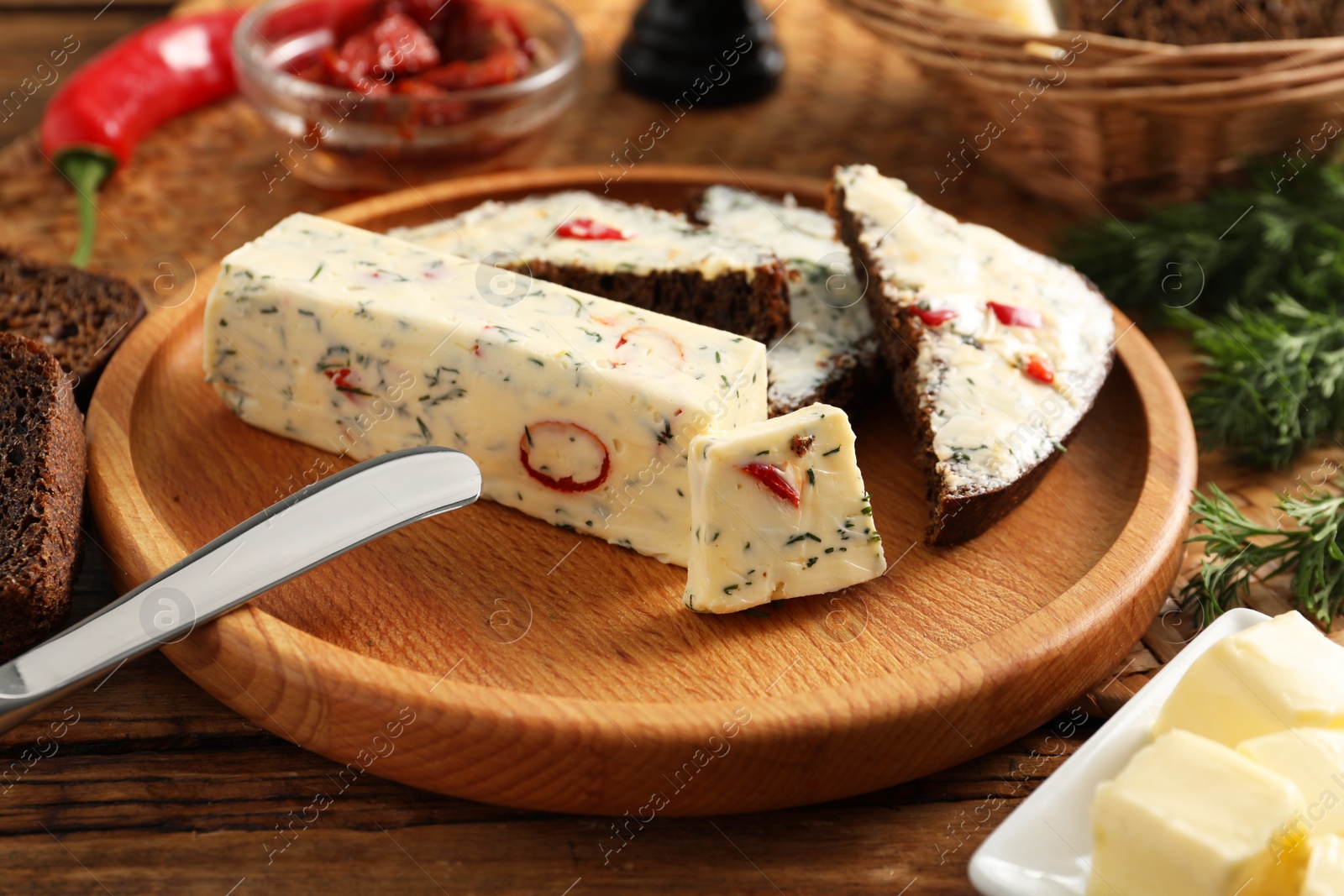 Photo of Tasty butter with dill, chili pepper and rye bread on wooden table