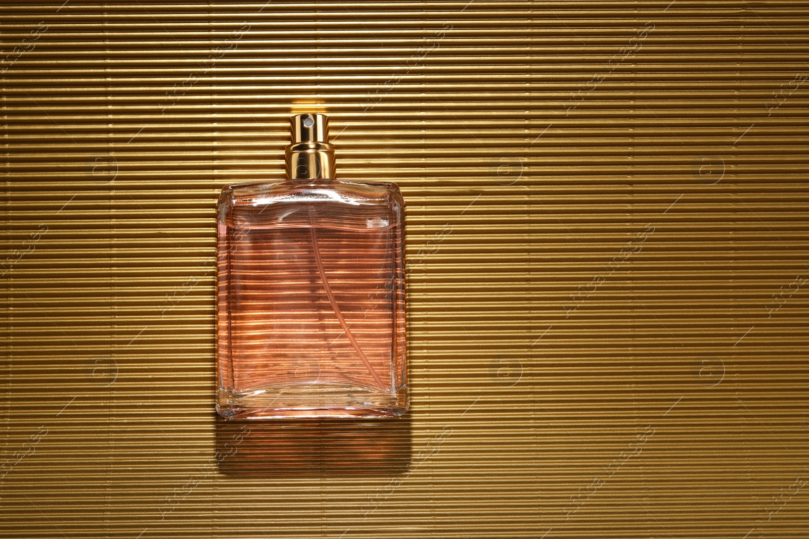 Photo of Luxury women's perfume. Sunlit glass bottle on golden surface, top view. Space for text