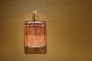 Luxury women's perfume. Sunlit glass bottle on golden surface, top view. Space for text