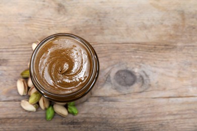 Photo of Tasty pistachio nut paste in jar on wooden table, top view. Space for text