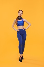 Young woman in sportswear and headphones on yellow background