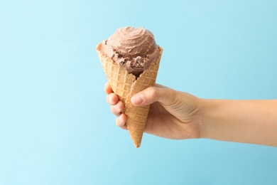 Photo of Woman holding waffle cone with delicious chocolate ice cream on light blue background, closeup