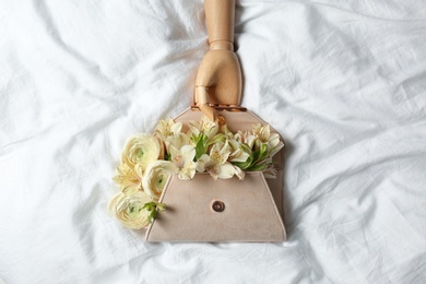 Photo of Stylish clutch with spring flowers and wooden mannequin hand on crumpled sheet, flat lay