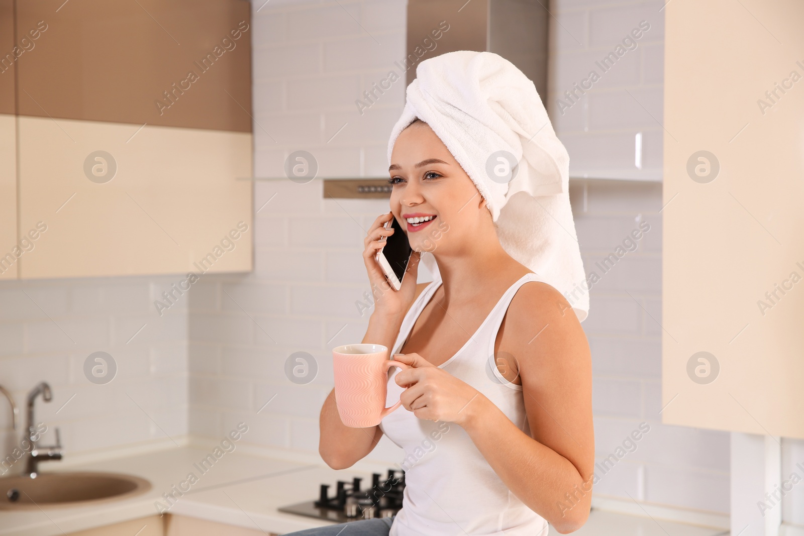 Photo of Beautiful woman with head wrapped in towel drinking tea and talking on phone at home