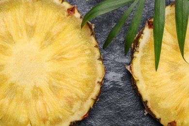 Slices of tasty ripe pineapple and green leaves on black textured table, closeup