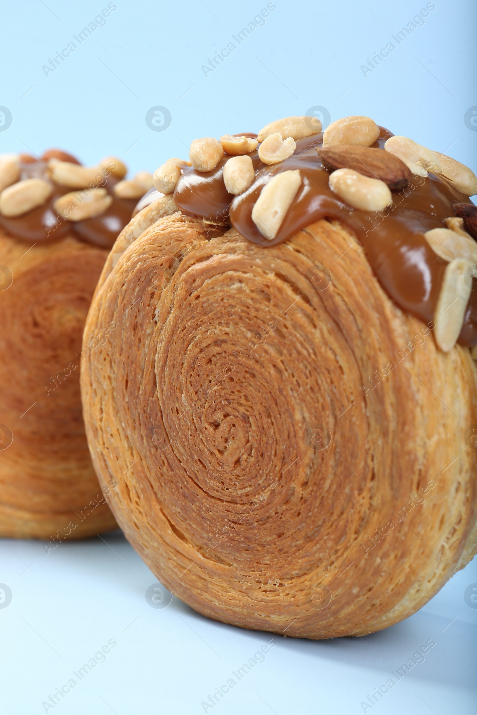 Photo of Supreme croissants with chocolate paste and nuts on light blue background, closeup. Tasty puff pastry